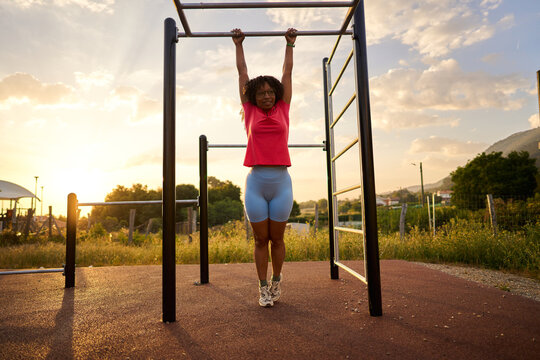 Woman training calisthenics on pull up bar at sunset