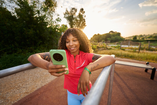 Woman smiling while using smartphone in park at sunset