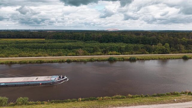 Cargo barge navigates Mittellandkanal in Germany under dramatic cloudy sky, representing inland freight transport. European waterway links major logistics routes toward Netherlands and Poland