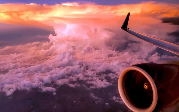 Aerial view of a commercial airplane engine and wing silhouetted against a massive, glowing cumulonimbus cloud illuminated by the warm light of a sunset over Pakistan.