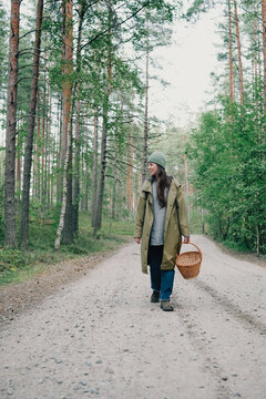 Woman carrying a wicker basket while walking along a forest road on her way to search for wild mushrooms during a seasonal mushroom picking trip in nature