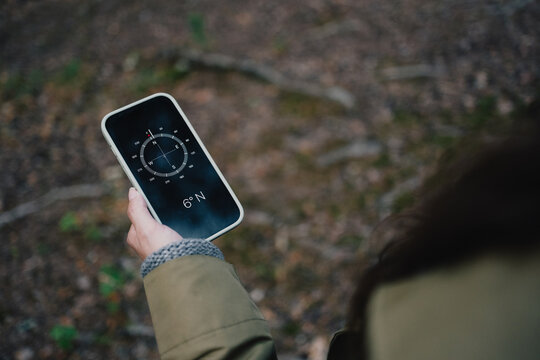 Woman using a digital compass on smartphone for navigation and finding direction while exploring a forest