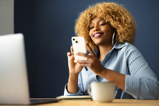 Woman Using Smartphone in Office With Laptop and Cup of Coffee