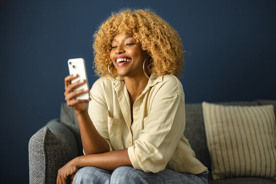 Woman Smiles While Using Smartphone on Couch in Cozy Living Room