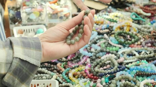 female hand holding grey agate bracelet at busy market stall. tourist choosing natural stone bracelet for souvenir gift. buying beautiful bracelet at local bazaar for daily fashion wear