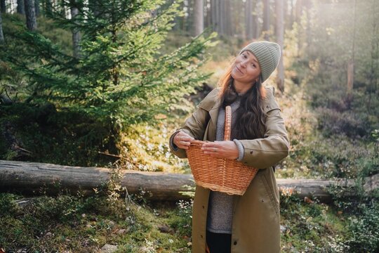Woman holding an empty wicker basket in a sunlit forest, ready for seasonal foraging and gathering wild food during a peaceful autumn nature outing