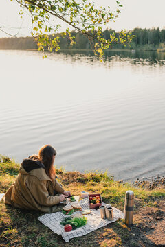 Woman preparing a picnic meal beside a peaceful lake, enjoying outdoor cooking and a relaxing weekend nature getaway during a warm seasonal afternoon