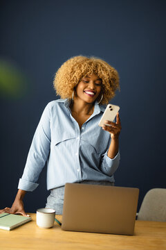Woman Smiles While Using Smartphone at Desk in Home Office