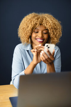 Woman Smiles While Using Her Smartphone at a Desk in an Office