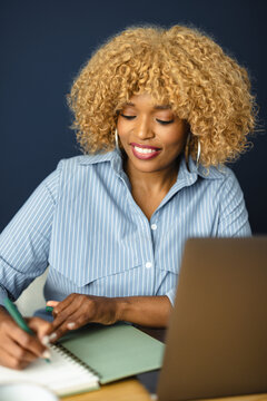 Woman Writes Notes at Work Desk With Laptop and Notepad