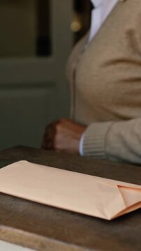 Vertical video: Placing envelope, man smoothing it at home wearing cardigan to secure mail