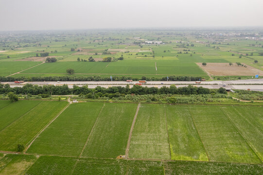 Aerial view of the Eastern Peripheral Expressway cutting through lush green agricultural fields and farmland in Dasna, Uttar Pradesh, India.