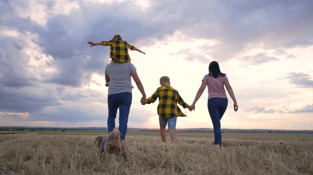 Happy cute family. Hiking outdoors in wheat field. Family walk together holding hands in natural park. Picnic in countryside at sunset. Children with parents walk with pet. Summer outdoor recreation.