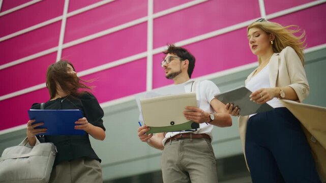 Three business professionals discuss work outside a contemporary building. They are collaborating and communicating in an urban environment.