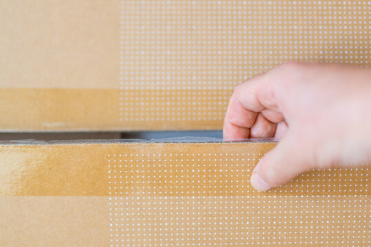 Hand pulling open taped cardboard box flap for packing and unboxing background and packaging banner shot