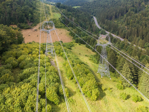 Aerial view of Korytnicka dolina valley featuring high-voltage power lines and electricity pylons stretching across lush green forests in Liptovska Osada, Zilinsky kraj, Slovakia.