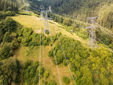 Aerial view of Korytnicka dolina valley featuring high-voltage power lines and steel pylons stretching across a lush green forested landscape in Liptovska Osada, Zilinsky kraj, Slovakia.