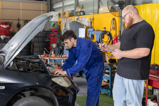Mechanic checks car engine while customer looks on inside auto repair shop
