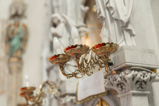 Candle holders glow during a holy mass in a catholic church. Participants witness the religious ceremony at the altar.