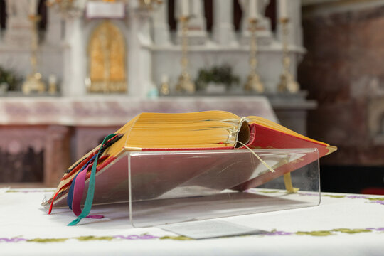 A religious ceremony takes place at a catholic church. An open holy bible book lies on the altar. People gather for holy mass.