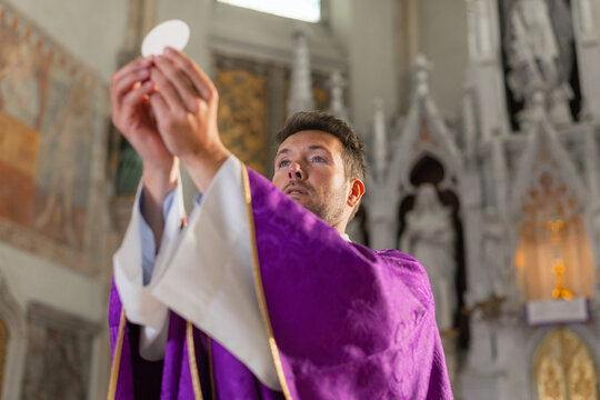 A catholic priest holds up the communion host during a holy mass in a church in Europe. The service is part of a religious ceremony.