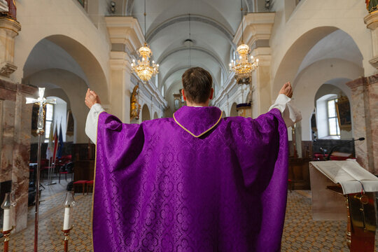 A priest stands with arms raised in a catholic church during holy mass. The service takes place in a European location.
