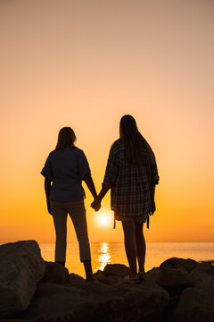 Two People Holding Hands on Rocky Shore at Sunset