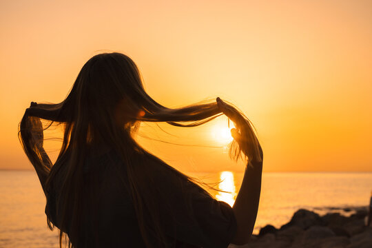 Silhouetted Woman Holding Long Hair Before Sunset