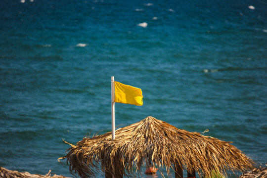 Thatched Beach Umbrella with Yellow Flag Above Blue Sea