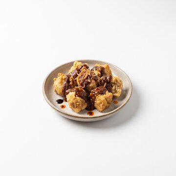 Crispy Indonesian batagor fried fish dumplings with savory peanut sauce on a plate isolated on white background