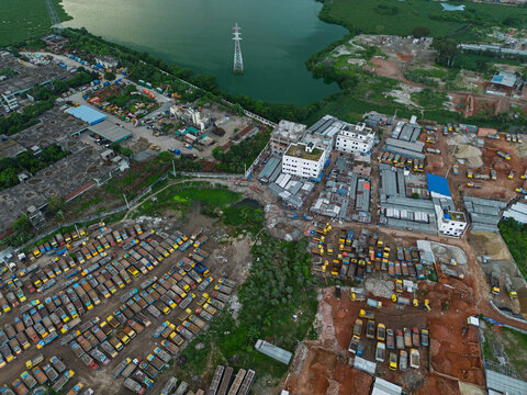 Aerial view of a logistics site in Dhaka with rows of parked trucks, industrial buildings, and an electricity pylon in the water, Dhaka, Dhaka Division, Bangladesh.