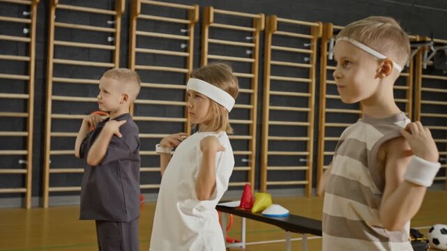 Caucasian children doing physical exercises in school gym, rotating shoulders and stretching arms up. Ideal for physical education videos, youth fitness campaigns, and healthy lifestyle ads