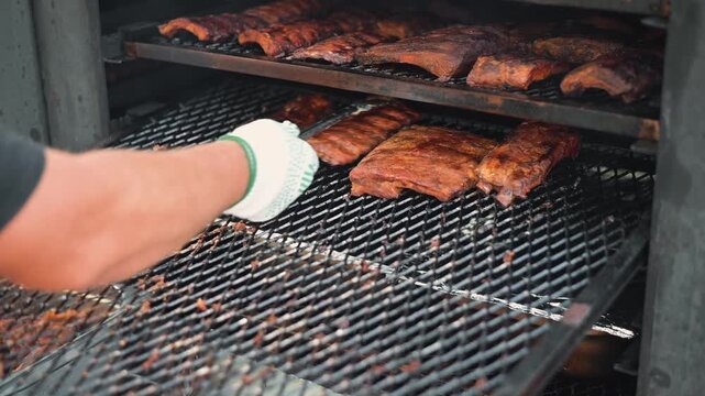 A hand adjusts the ribs on a grill while smoke rises in the air. This cooking activity takes place outdoors, showcasing the process of grilling meat
