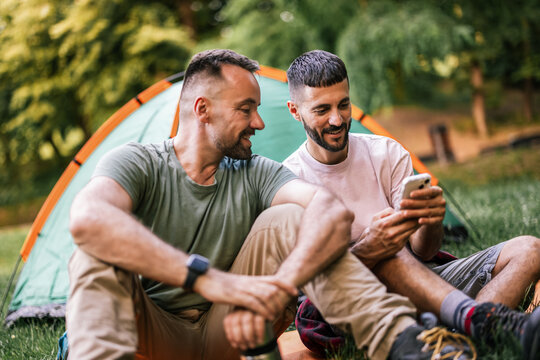 Gay couple sharing a moment while viewing a smartphone beside a camping tent