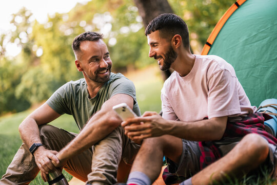 Gay couple using a smartphone while relaxing beside their camping tent outdoors