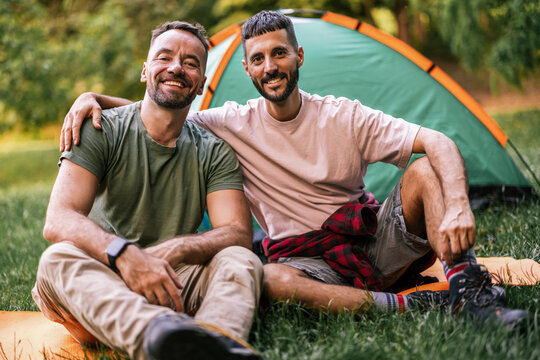 Gay couple sitting together and smiling with arms around each other outdoors