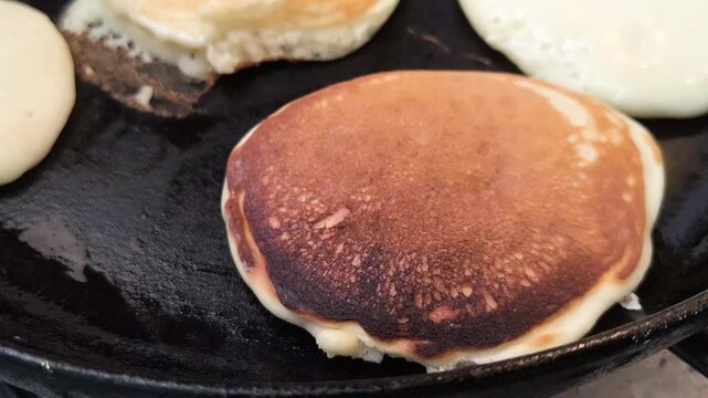 Cooking fluffy homemade pancakes in a hot cast iron skillet, flipping golden brown pancakes with a fork during preparation.