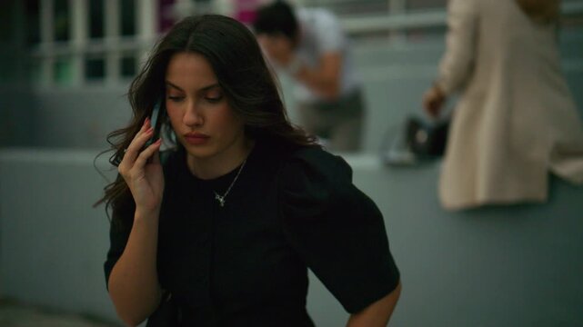 A young business woman is deeply engaged in a phone conversation outdoors. She appears focused and serious while talking on her mobile phone in an urban environment.