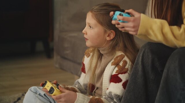 Focused girl and her sister play video game with gamepads at home