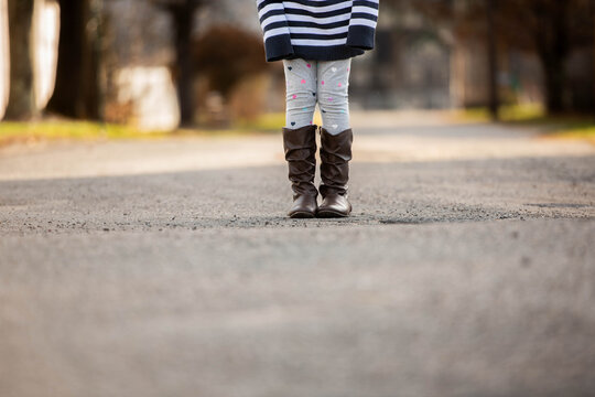 Tween girl stands alone in the middle of the road, wearing a striped sweater and slouch boots, with no face visible, evoking independence, transition and growing up.