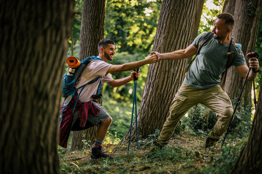Two hikers helping each other navigate uneven terrain in a forest