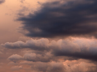 Fototapeta premium Dramatic dark storm clouds illuminated by warm orange sunset light, creating a moody atmospheric cloudscape before a possible thunderstorm.