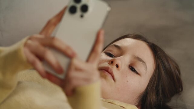 Bored girl scrolls social media on phone while lying on couch, excessive use