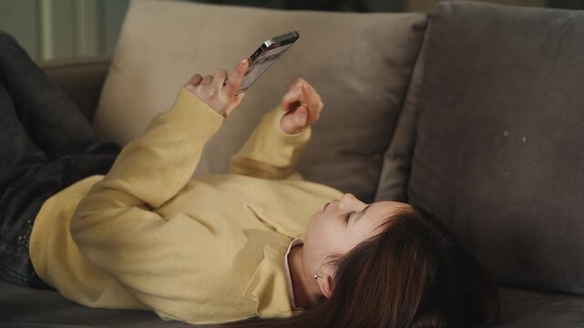 Girl scrolls social media on phone while lying on sofa, excessive screen time