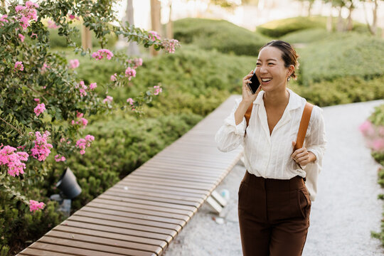 Smiling Korean woman walks through the garden while enjoying a phone call