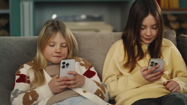 Two focused female friends scroll through phones on sofa, screen dependency