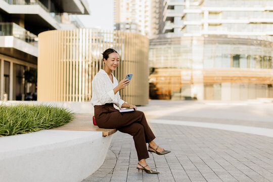 Korean woman enjoying a sunny day while using her smartphone in a modern setting