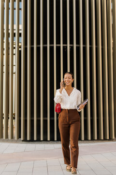 Korean woman walking confidently while making a phone call on a sunny day