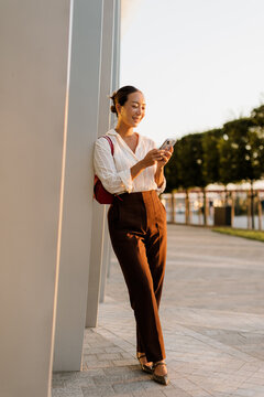 Korean woman enjoys sunny evening while checking her smartphone outside