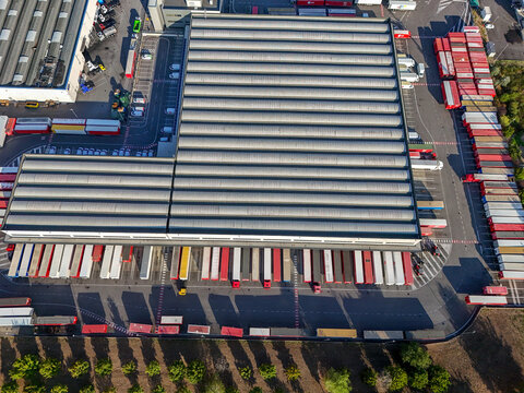Aerial view of a large logistics warehouse and freight forwarding facility with numerous semi-trailers parked at loading bays in Settimo Torinese, Piedmont, Italy.